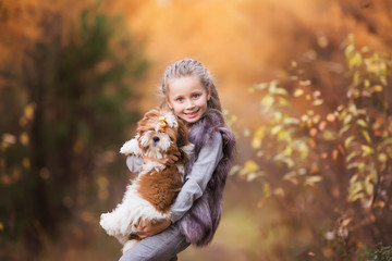 Portrait of a cute young girl in a fur vest, embracing fluffy puppy in autumn park