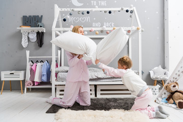 cute mother and daughter in pajamas fighting with pillows