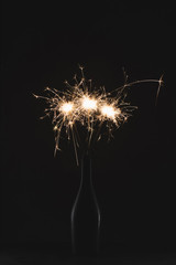 close up view of burning sparklers in bottle isolated on black