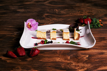 Close up of creamy mascarpone delicious cheesecake with strawberry, chocolate and berries, decorated by orchid flower. New York cheesecake. Christmas dessert. Healthy food. Wooden background