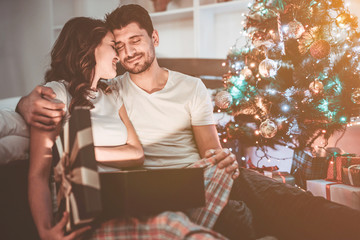 The happy couple sit with a gift box near the christmas tree