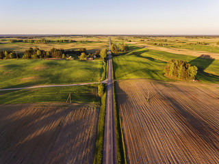 Aerial view over rural village with agricultural green fields in Lithuania, during sundown.
