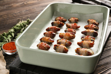 Ceramic baking dish with bacon wrapped dates on wooden background