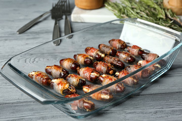 Glass baking dish with bacon wrapped dates on wooden background
