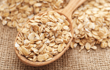 Oatmeal flakes and spoon on sackcloth fabric, closeup