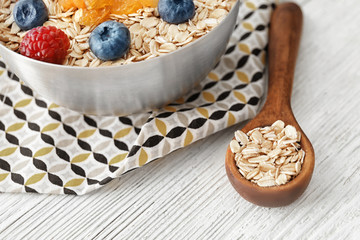 Spoon and bowl with oatmeal flakes on wooden background
