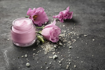 Jar of body cream and flowers on grey background