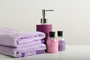 Clean towels and cosmetics on table against light background