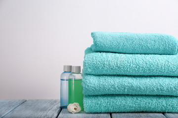 Clean towels and cosmetics on table against light background