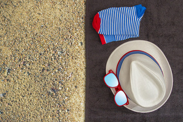 Fototapeta na wymiar Male set of things for summer holidays (hat, sunglasses, socks) on a on a dark towel and yellow sand background. Top view. 