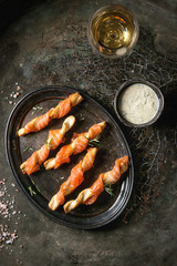 Appetizer with smoked salmon on crispy breadsticks served on vintage metal tray with cheese dill sauce, sea salt, glass of white wine over old dark background. Top view with space