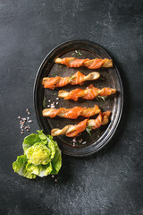 Appetizer with smoked salmon on crispy breadsticks served on vintage metal tray with sea salt and green salad over black texture background. Top view with space