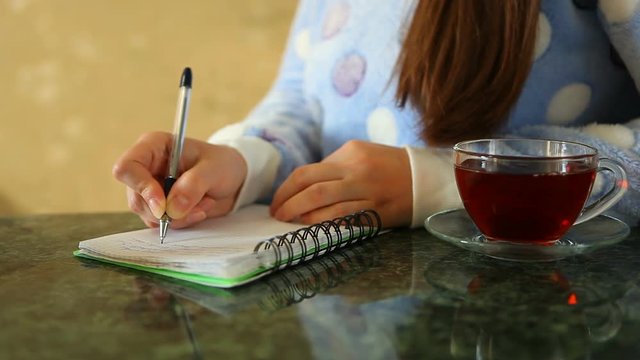 Woman writing in journal, with cup of tea on the table