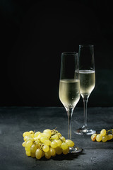 Two glasses of white champagne served with green grapes over dark texture background. Copy space