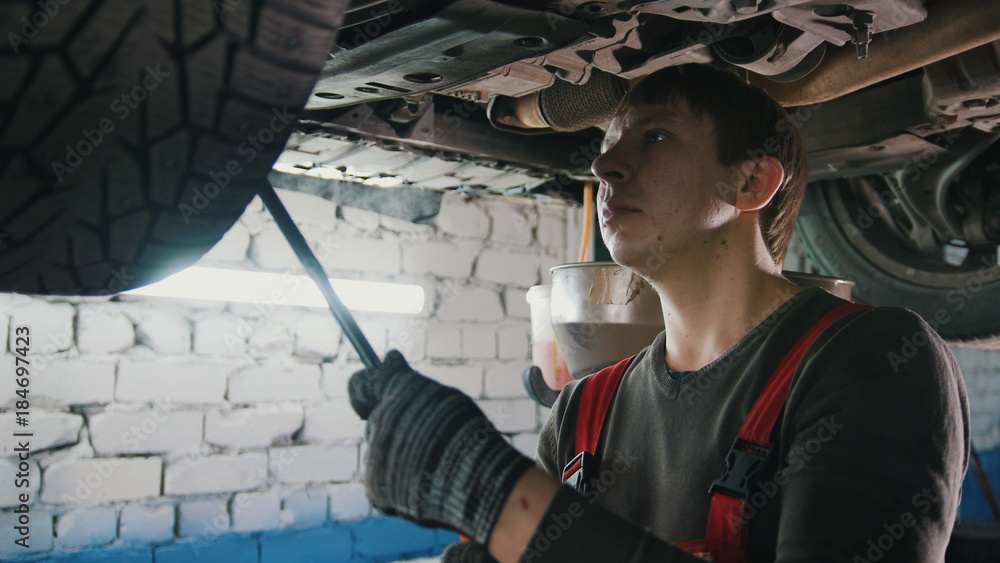 Wall mural mechanic with the lamp is checking the bottom of car in garage automobile service, close up