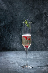 One glass of white champagne served with red berries and rosemary over blue texture background. Copy space