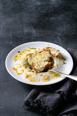 Traditional french onion soup with cheese and bread served in white ceramic plate with rosemary, spoon and textile napkin over black texture background.
