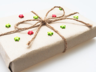A present or gift box wrapped by rough brown recycled paper and tied with brown hemp rope as ribbon with red and green star  isolated on white background with concept of green and environment friendly