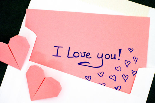 Letter with text I Love You! in envelope and two pink origami hearts.
