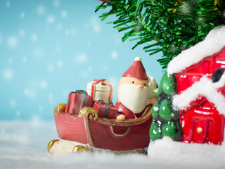 Happy Santa Claus with gifts box on the snow sled going to house. near house have Snowman and Christmas Tree. Santa Claus and house on the snow. Christmas and happy new year concept.