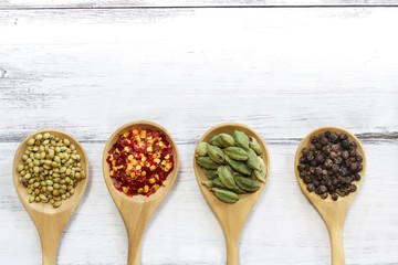 Various spices in wooden spoon on dark black background, top view