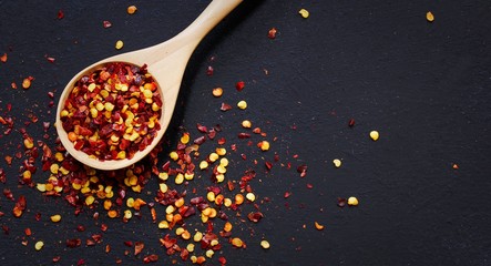 Red Chilli flakes in wooden spoon on dark black background,top view copy space