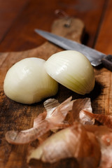 Onion cut in half on cutting board. Onion shells in the foreground and cut knife in the background.