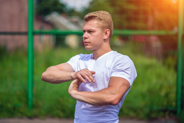 A male athlete goes in for sports in the open air. Muscular arms. Blonde in a white T-shirt. Lifestyle of the bodybuilder