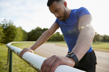 Male athlete leaning on fence at running track, close up
