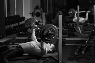 Brutal athletic man pumping up muscles on bench press, black and white