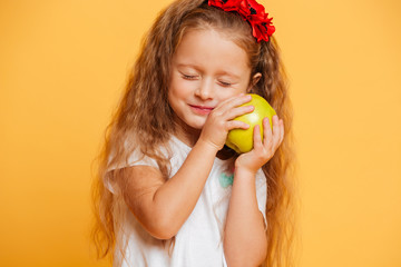 Cheerful little girl child holding apple with eyes closed.