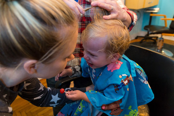 Caucasian Toddler Boy Has His Hair Cut By A Barber As His Mom Watches