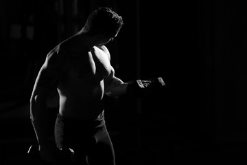 Handsome power athletic guy bodybuilder doing exercises with dumbbell. Fitness muscular body on dark background. black and white