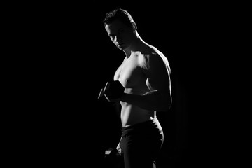Handsome power athletic guy bodybuilder doing exercises with dumbbell. Fitness muscular body on dark background. black and white