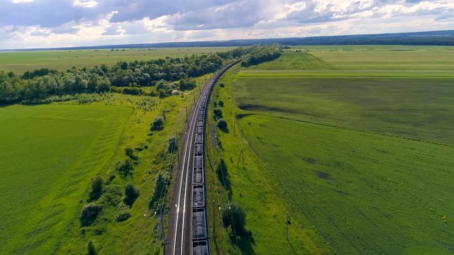 Aerial shot of cargo train in green field. 4K.