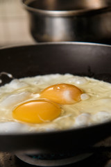 Two eggs frying in teflon skillet with defocused aluminum pan in background.