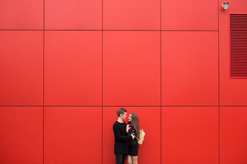 Young man and woman in passion, emotion, on the street with a backdrop of the red wall. Fashion