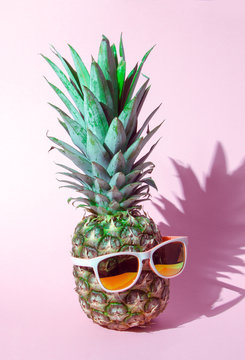 Creative layout made of summer tropical fruits and leaves. Pineapple in glasses on a pink icolated bacground. Flat lay. Food concept.