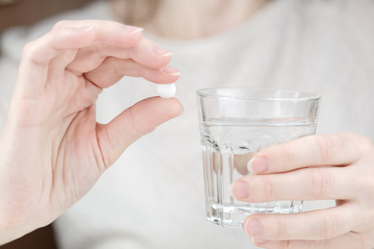 сlose-up View Photo Of Female Hands Holding One White Round Pill And Glass Of Water. Young Woman Taking Medication, Feeling Ill. Healthcare Concept