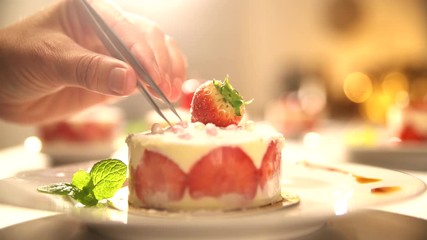 Close-up on the hand of a pastry chef depositing a pearl of sugar on a strawberry cake