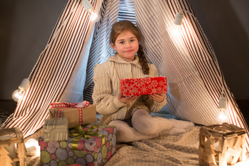 Beautiful little girl sitting with a present in his hands. Deploy Christmas gift box on holiday in...