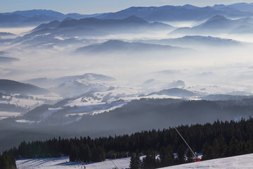 View from the ski slopes  on snow covered and foggy valley on the background mountain peaks. © anatoliil