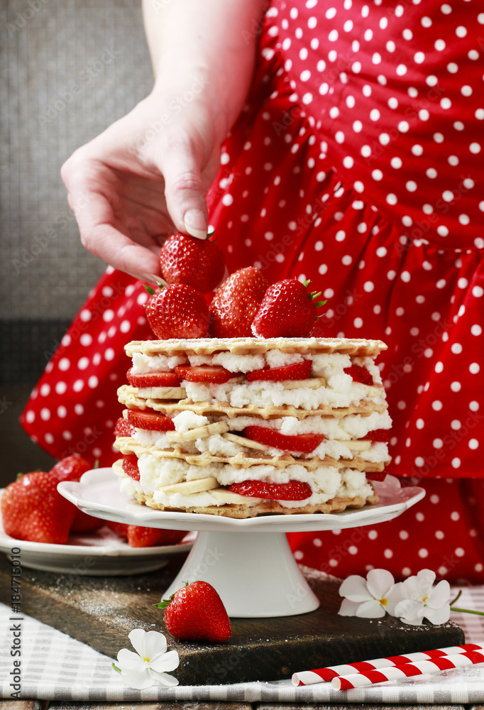 Sticker woman decorating strawberry layer cake with fresh fruits.