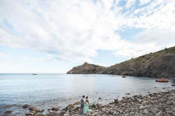 The bride and groom on nature in the mountains near the water. Suit and dress color Tiffany. Stand on the beach holding hands.