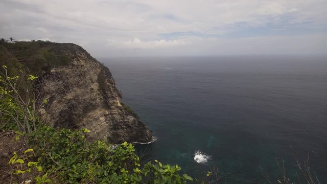 Cliff with waves crashing against rocky shore, Nusa Penida, Indonesia. Rocky coast and ocean with waves and rocky cliff. 4K video. Travel concept.