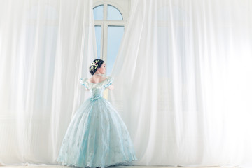 Elegant woman at a high window in historic dress, straightens the curtains, and waiting for friends...