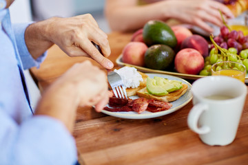 man with fork eating bacon at table full of food