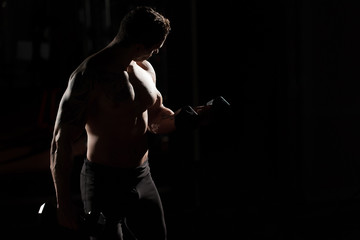Fototapeta na wymiar Handsome power athletic guy bodybuilder doing exercises with dumbbell. Fitness muscular body on dark background.