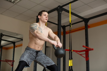 Fototapeta na wymiar Beautiful man squats with kettlebell at the gym