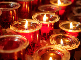 Close-up detail of multiple lit votive candles in red glass holders lighting up a church, during a mass. Valencia, Spain. Travel and religion concept.